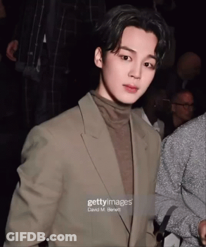 A Man In A Suit And Turtleneck Is Standing In Front Of A Crowd GIF