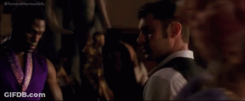 A Man In A Suit And Vest Is Looking At The Camera While Standing In A Crowded Room . GIF