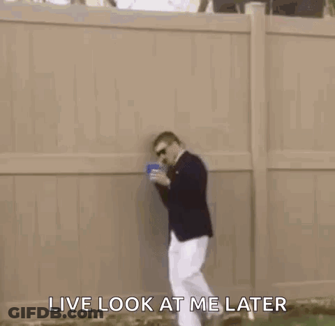 A Man In A Suit And White Pants Is Standing In The Grass Holding A Blue Cup . GIF