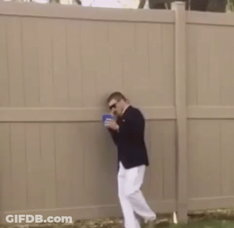 A Man In A Suit And White Pants Is Standing Next To A Fence In The Grass . GIF