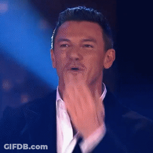 A Man In A Suit And White Shirt Is Clapping His Hands On A Stage . GIF
