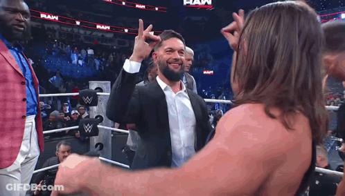 A Man In A Suit And White Shirt Is Giving A High Five To Another Man In A Wrestling Ring . GIF