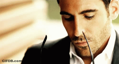 A Man In A Suit And White Shirt Is Holding A Pair Of Glasses In His Mouth . GIF