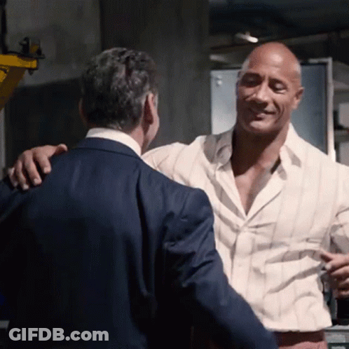 A Man In A Suit And White Shirt Is Hugging Another Man GIF