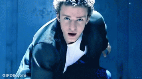 A Man In A Suit And White Shirt Is Kneeling Down In Front Of A Blue Wall . GIF