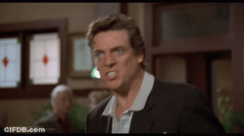 A Man In A Suit And White Shirt Is Making A Funny Face In Front Of A Window . GIF