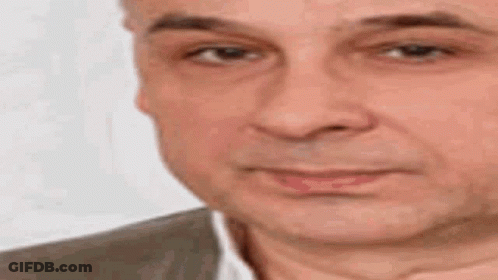 A Man In A Suit And White Shirt Is Making A Funny Face With His Hand On His Chin . GIF