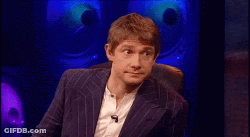 A Man In A Suit And White Shirt Is Sitting In A Chair In Front Of A Microphone . GIF