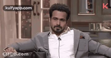 A Man In A Suit And White Shirt Is Sitting In A Chair With His Hands On His Knees . GIF