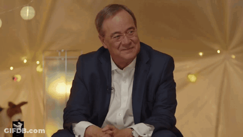 Man In Suit Sitting In Front Of A Sign GIF