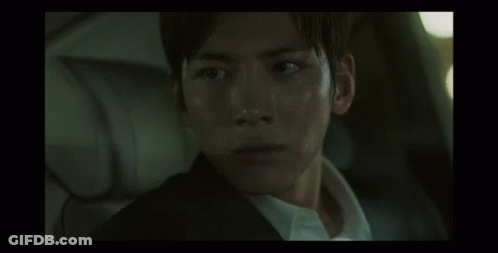 A Man In A Suit And White Shirt Is Sitting In The Back Seat Of A Car And Looking At The Camera . GIF