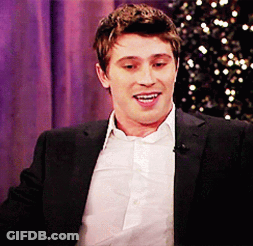 A Man In A Suit And White Shirt Is Smiling In Front Of A Purple Curtain GIF
