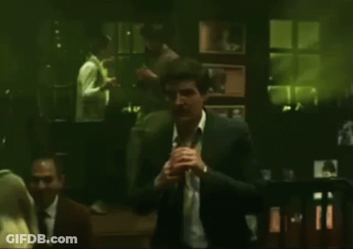 A Man In A Suit And White Shirt Is Standing In A Dark Room With A Green Background . GIF