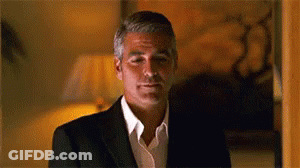 A Man In A Suit And White Shirt Is Standing In A Room And Looking At The Camera . GIF