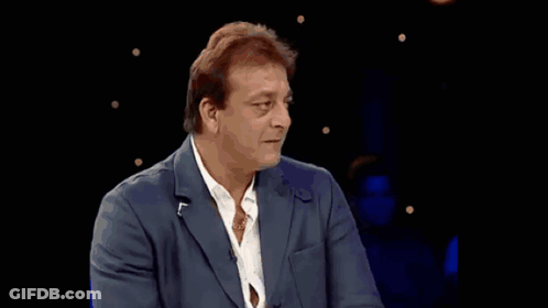 A Man In A Suit And White Shirt Is Standing In Front Of A Crowd GIF