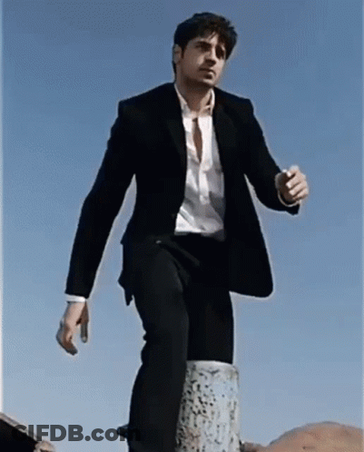 A Man In A Suit And White Shirt Is Standing On A Post GIF
