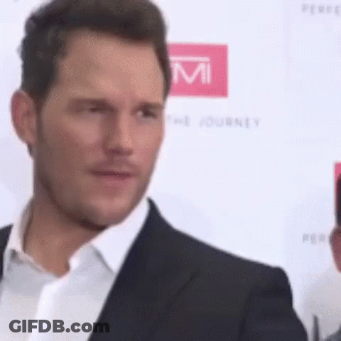A Man In A Suit And White Shirt Is Standing On A Red Carpet And Looking At The Camera . GIF