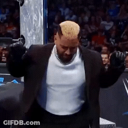 A Man In A Suit And White Shirt Is Standing With His Arms Outstretched In Front Of A Crowd . GIF