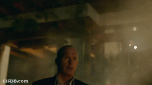 A Man In A Suit And White Shirt Stands In A Dark Room GIF