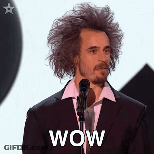 A Man In A Suit And White Shirt Stands In Front Of A Microphone With The Word Wow On His Face GIF