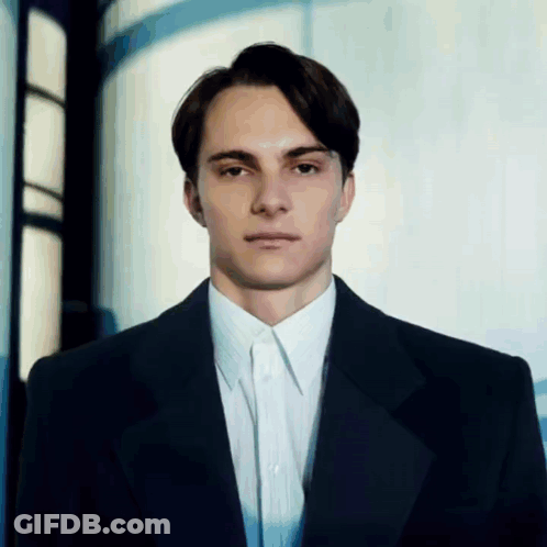 A Man In A Suit And White Shirt Stands In Front Of A Window GIF