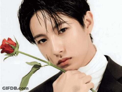 A Man In A Suit And White Turtleneck Holds A Red Rose To His Face GIF