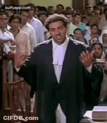 A Man In A Suit And Wig Is Standing In Front Of A Crowd In A Courtroom . GIF