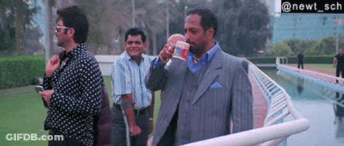 A Man In A Suit Drinking From A Cup That Says ' Noodles ' On It GIF