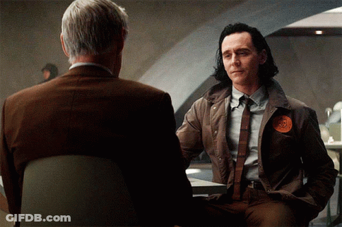 A Man In A Suit Has A Patch On His Jacket That Says ' Loki ' GIF