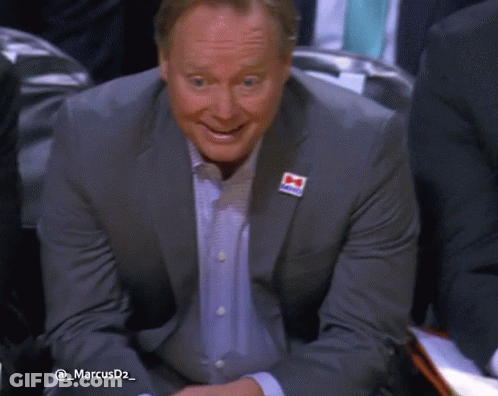 A Man In A Suit Has A Red White And Blue Ribbon On His Jacket With The Letter M On It GIF