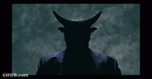 A Man In A Suit Has Horns On His Head In A Dark Room GIF