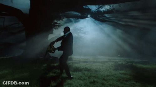A Man In A Suit Holding A Chainsaw In A Dark Forest GIF