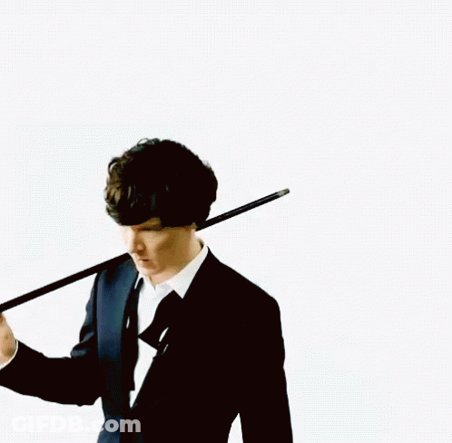 A Man In A Suit Holds A Cane Over His Shoulder GIF