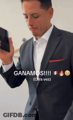 A Man In A Suit Holds A Cell Phone And Says Ganamos GIF