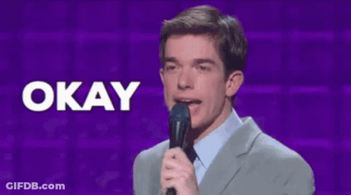 A Man In A Suit Holds A Microphone In Front Of A Sign That Says Okay GIF