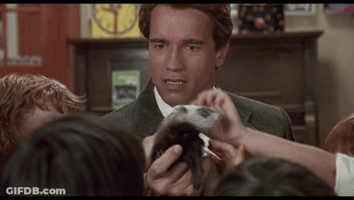 A Man In A Suit Holds A Small Animal In Front Of A Group Of Children GIF