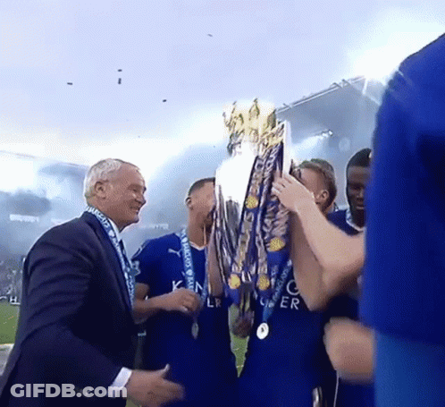 A Man In A Suit Holds A Trophy In Front Of A Group Of Soccer Players In Blue Jerseys GIF