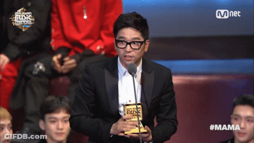 A Man In A Suit Holds A Trophy In Front Of A Microphone At A Music Awards GIF