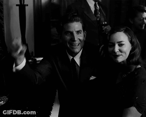 A Man In A Suit Holds Up A Cigar Next To A Woman GIF