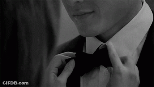 A Man In A Suit Is Adjusting His Bow Tie In A Black And White Photo GIF