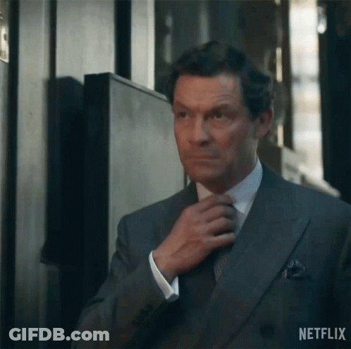A Man In A Suit Is Adjusting His Tie In A Hallway . GIF
