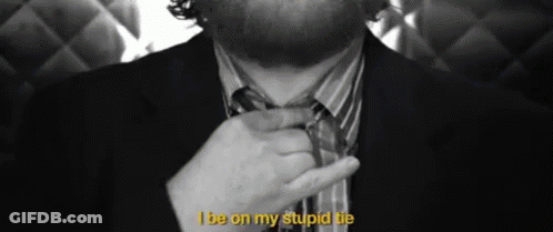 A Man In A Suit Is Adjusting His Tie With The Words I Be On My Stupid Tie Above Him GIF
