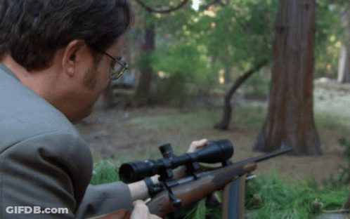 A Man In A Suit Is Aiming A Rifle With A Scope GIF