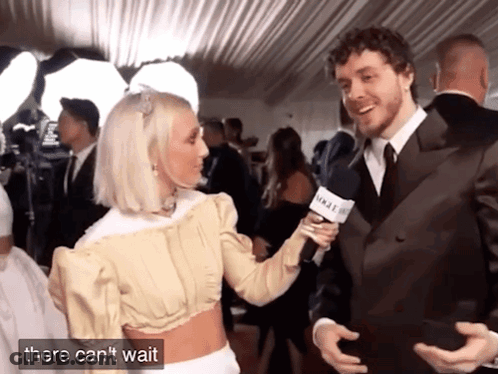 A Man In A Suit Is Being Interviewed By A Woman Who Is Holding A Microphone That Says Vogue GIF