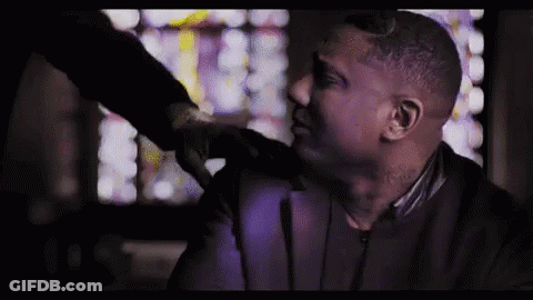 A Man In A Suit Is Being Punched In The Face By Another Man In A Dark Room . GIF