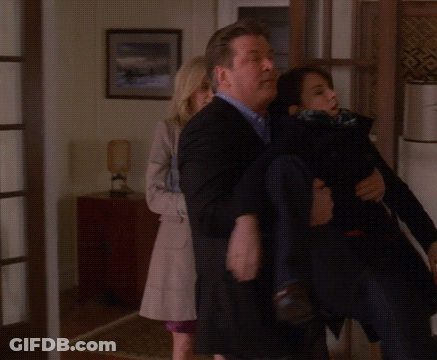 A Man In A Suit Is Carrying A Woman In A Black Coat GIF