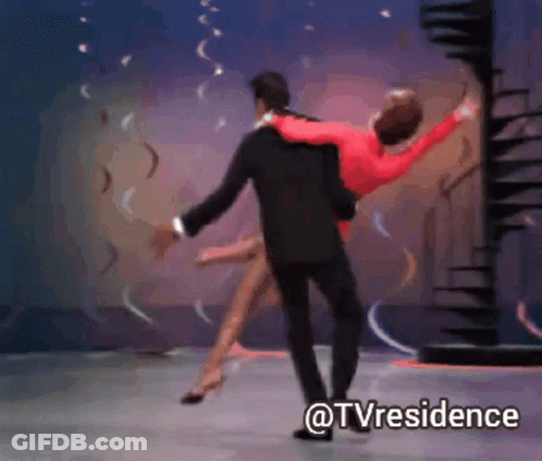 A Man In A Suit Is Carrying A Woman In A Red Dress On A Stage With The Words @Tvresidence Below Them GIF