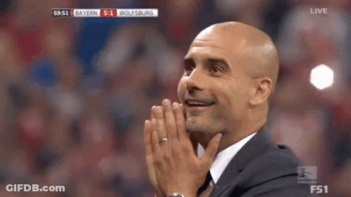 A Man In A Suit Is Covering His Face With His Hands While Watching A Soccer Game Between Bayern And Wolfsburg . GIF