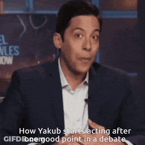 A Man In A Suit Is Covering His Mouth With His Hand While Talking About Yakub GIF