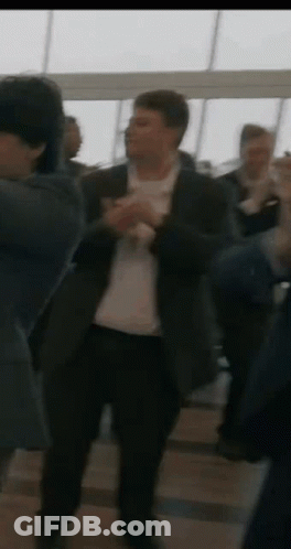 A Man In A Suit Is Dancing In A Crowd Of People In A Room . GIF